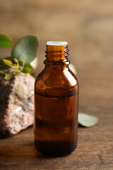 Bottle of eucalyptus essential oil, stone and leaves on wooden table
