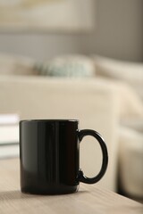 Black mug on wooden table indoors. Mockup for design