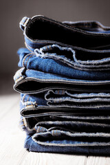 Worn denim trousers. Machine stitch close up. Denim texture in blue. The concept of repairing old clothes. Sewing factory. Fashionable aging clothes. Stack of jeans. 