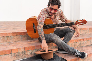 Latin man sitting on the sidewalk playing guitar for money