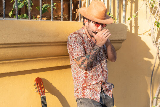 Young scruffy musician plays his harmonica on the street - Powered by Adobe
