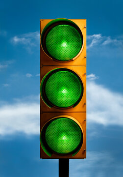 Vertical Closeup Shot Of A Traffic Light With All Green Lights Against The Blue Sky