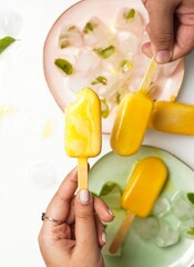 Vertical shot of mango ice cream popsicles on pastel-colored plates with ice.