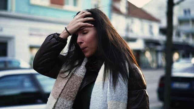 Worried young woman walks in street shaking head in disbelief. Preoccupied female person in 20s feeling frustration and stress during difficult times