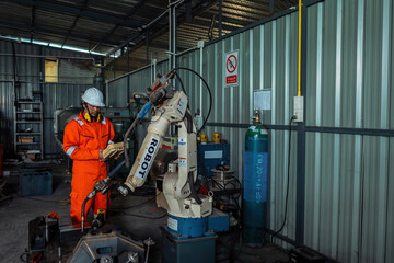 Male engineer holding robot controller for maintenance or repair automatic robotic machine in factory. Male technician worker working with control automatic robot arm system welding in the factory