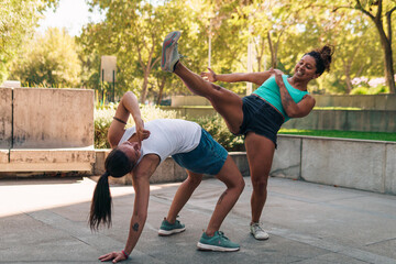 mujeres divirtiéndose en la ciudad practicando capoeira en un día soleado tirando patadas y...