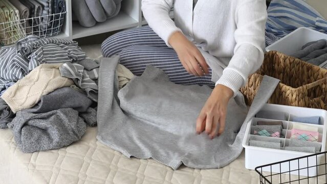 The concept of organizing and storing clothes. A woman folds a sweater and a T-shirt and puts it in a basket.