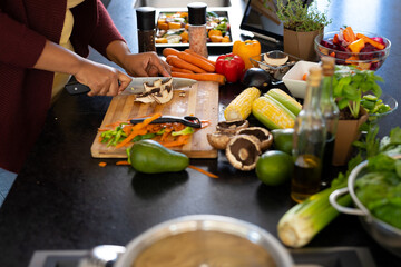 Midsection of plus size african american woman preparing dinner, chopping vegetables in kitchen