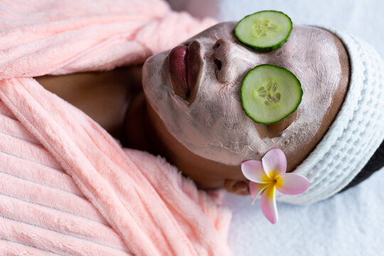 Relaxed plus size african american woman with beauty face mask and cucumber slices on eyes at spa