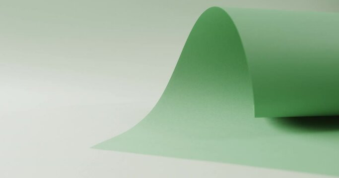 Close up of green rolled piece of paper on white background with copy space in slow motion