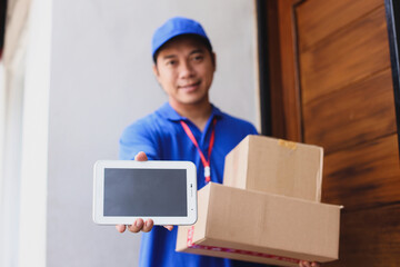 Smiling deliveryman in blue uniform with cap holds parcels to send while showing blank screen of smartphone for mock up. 