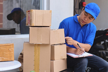 Courier in blue uniform with cap checking parcels and writing notes before send to customer