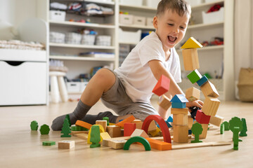 Smiling male kid playing with natural wooden bricks toys construction tower Montessori material