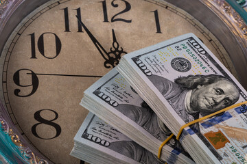 100 American dollar bills and the dial of a large wall clock