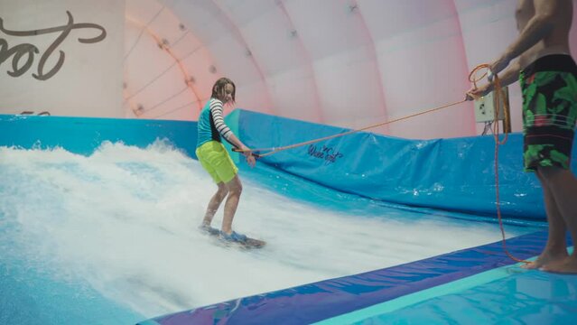 Water sport activity, balance concept. Little athlete enjoying indoor surfing. Teenager rides board on waves on simulator in sports complex. Surfing coach and student in session on wave simulator.