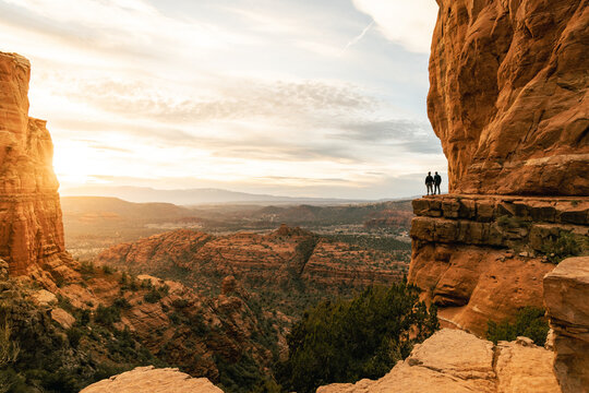 Young heterosexual couple holds hands at viewpoint during dramatic sunset from Cathedral Rock in Sedona.