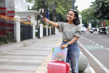 Pretty Asian woman in casual style bring luggage and map taking a selfie and make a vlog while traveling a place. 
