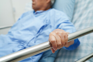 Asian elder senior woman patient holding bed rail while lie down with hope waiting her family in hospital.