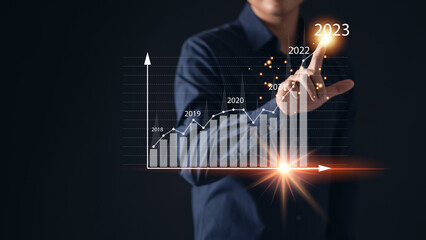 Man using his hand to point at a business growth graph with the number 2023, representing the concepts of trend, development, progress, and success in the pursuit of goals and objectives