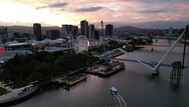 Drone shot of South Bank, shot over Brisbane River, Static shot facing The Wheel of Brisbane. Citycat Boats approaching South Bank pontoon. New Neville Bonner Bridge in construction in background
