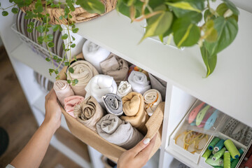 Woman seamstress choosing fabric textile material neatly folded eco basket electric sewing machine
