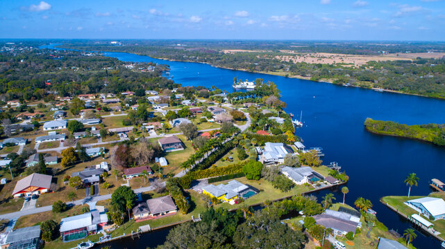 Real Estate Homes on a River in Bonita Springs, Florida Lined by Foliage and Luxury Real Estate, Featuring Clear Sky and Light Clouds