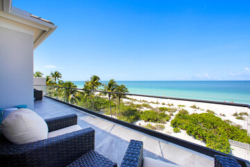 Beach View Balcony with Palm Trees, Sand, and Clear Blue Sky in Naples, Florida Overlooking Calm Ocean Waters