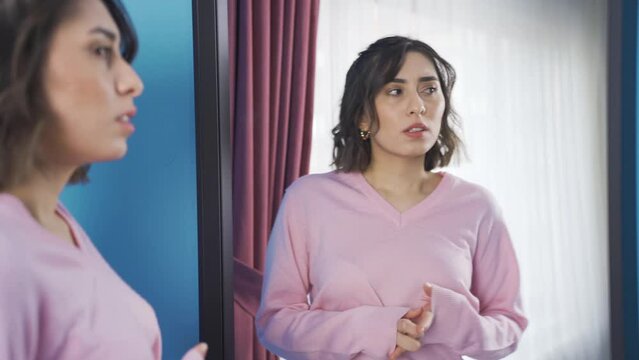 Angry young woman who finds herself guilty in front of mirror.
Young woman talking to herself at home blames herself and finds fault.
