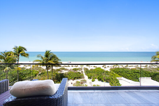 Beach View Balcony with Palm Trees, Sand, and Clear Blue Sky in Naples, Florida Overlooking Calm Blue Ocean Waters
