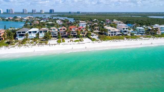 Drones Eye View of Homes on Bonita Springs Beach in Florida with Clear Water Crashing Waves in the Foreground and Bay Waters Surrounded by Mangroves in the Background