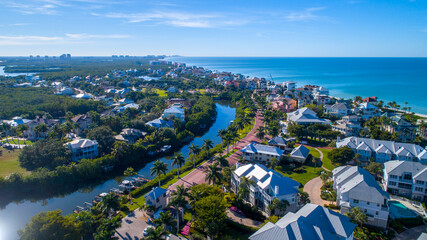 Aerial Perspective from Drone Featuring the Barefoot Beach in Bonita Springs, Florida. Blue Water Coastline with Clear Sky and Wispy Clouds in the Background and Clusters of Homes in the Foreground - obrazy, fototapety, plakaty