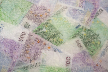 Blurred photo of one hundred and five hundred euros are defrosted in ice. The European cash currency is frozen.