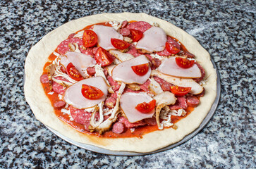 raw pizza with ingredients, tomatoes sausage ham, close-up