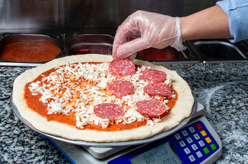Cooking pizza by the chef, puts sausage on the dough with sauce and mozzarella
