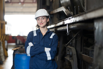 Female engineer worker working in industry factory, standing with crossed arms, happy and smiling, wearing safety uniform, helmet. Caucasian female technician worker at work in locomotive garage