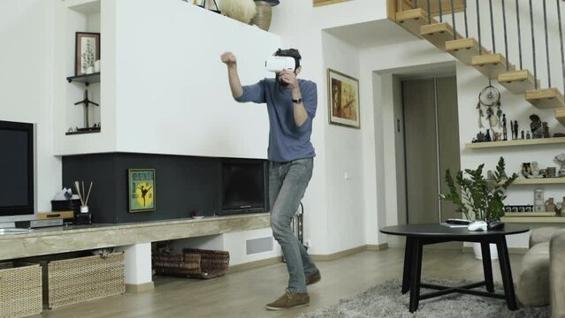 Guy looks fully involved into this future tecnology while playing VR game: he is boxing air with his hands, moving around in order to defend himself and to avoid strikes from his opponent.