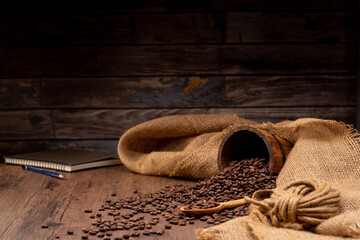 The many coffee beans are placed around on a wooden table in a warm, light atmosphere, on a dark background, with copy space.