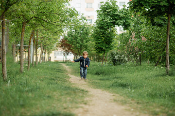 Fototapeta premium Child having fun and enjoy a weather. All kids love play with stick. Happy childhood. Cute curious boy standing in deep dark forest at old tree covered with green moss looking up waiting for magic
