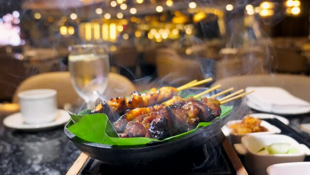 Satay chicken skewers cooked on the grill with smoke. Delicious Malaysian dish in a modern luxury restaurant. Skewered chicken grilled to perfection over charcoal. Fine dining food.