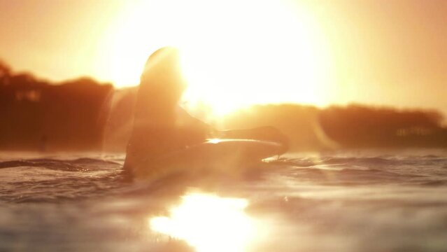 Slow motion ocean footage of a woman on a surfboard at sunset