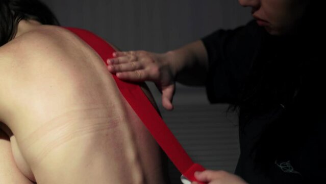The masseur sticks teips on the back of a young woman