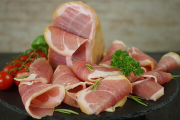 Traditional Italian smoked dry ham close-up composition with basil and tomato