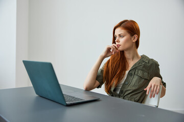 a woman in a large bright room sits at a laptop and seriously thinks about her work