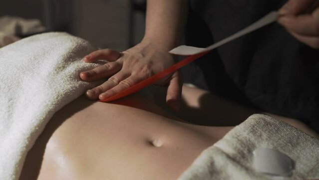The masseur sticks teips on the woman's stomach