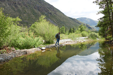 Fototapeta na wymiar A handsome man with a backpack in the mountains looking into a mountain river. Journey through picturesque places in the Altai Mountains. 
