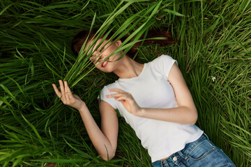 happy woman lies in tall grass covering her face with leaves