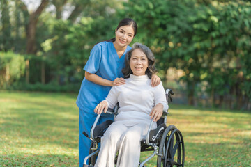 Young asian care helper with asia elderly woman on wheelchair relax together park outdoors to help and encourage and rest your mind with green nature. Looking camera.