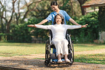 Young asian care helper with asia elderly woman on wheelchair relax together park outdoors to help and encourage and rest your mind with green nature. physical therapy