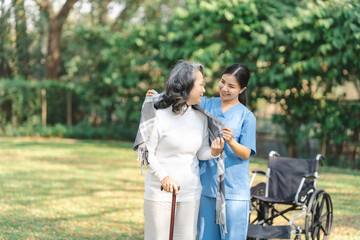 Fototapeta premium Young asian care helper with asia elderly woman on wheelchair relax together park outdoors to help and encourage and rest your mind with green nature. Wear a scarf over your shoulders with care.