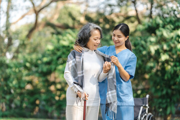 Young asian care helper with asia elderly woman on wheelchair relax together park outdoors to help...